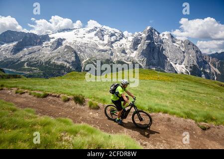 Ciclista con una mountain bike elettrica (e-bike) lungo il sentiero Viel del Pan (Bindelweg) di fronte alla Marmolada, Padon cresta ai confini Foto Stock