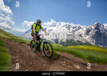 Ciclista con una mountain bike elettrica (e-bike) lungo il sentiero Viel del Pan (Bindelweg) di fronte alla Marmolada, Padon cresta ai confini Foto Stock