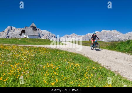 Donna con e-bike sulla strada sterrata vicino alla cappella di Sant'Antonio, altopiano di Pralongia, Dolomiti, Corvara, alta Badia , Alto Adige, Italia, Foto Stock