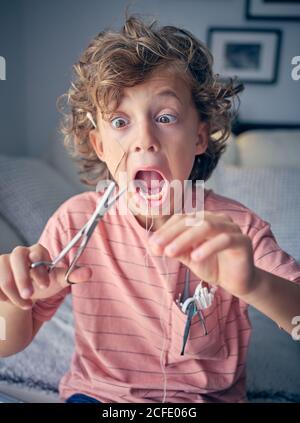 Eccitata ragazzina che tira il filo interdentale per cui il dente del latte legato con forbici in mano a casa Foto Stock