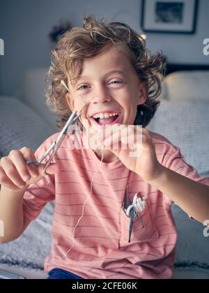 Eccitata ragazzina che tira il filo interdentale per cui il dente del latte legato con forbici in mano a casa Foto Stock