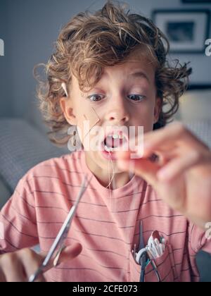 Eccitata ragazzina che tira il filo interdentale per cui il dente del latte legato con forbici in mano a casa Foto Stock