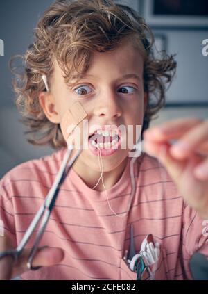 Eccitata ragazzina che tira il filo interdentale per cui il dente del latte legato con forbici in mano a casa Foto Stock