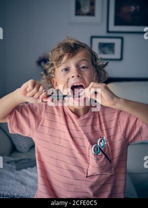 Eccitata ragazzina che tira il filo interdentale per cui il dente del latte collegato con le forbici in mano a casa guardando la fotocamera Foto Stock