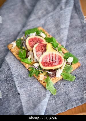 Delizioso panino all'aperto colorato fatto in casa con fette di fico e. pezzi di formaggio su pane di segale croccante tra verde aromatico foglie di insalata di razzo Foto Stock