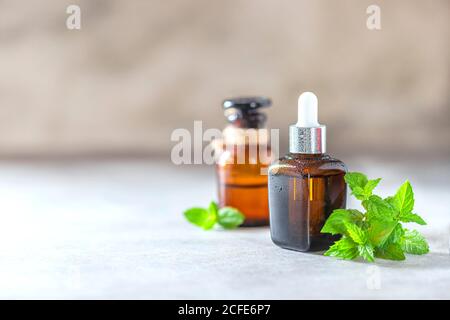 Cosmetici con estratto o olio di menta piperita. Olio essenziale di menta piperita e foglie su sfondo chiaro. Foto Stock