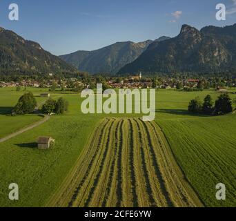 Veduta aerea della periferia di Oberammergau con Kofel sullo sfondo, chiesa parrocchiale di San Pietro e Paolo, prato, sentiero, in legno a doghe, Foto Stock