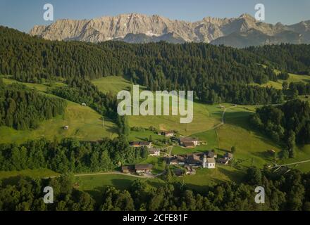 Vista aerea di Wamberg con la Chiesa di Sant'Anna contro i Monti Wetterstein nella luce della sera, sentiero, campo, prato, alberi, cielo blu, Foto Stock