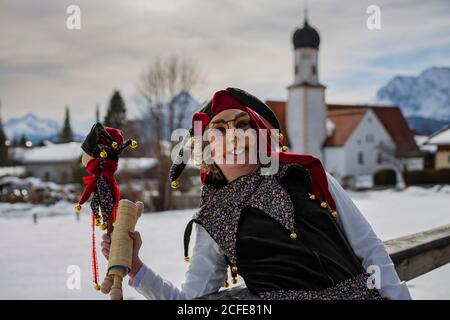 Ritratto di donna in costume di Mardi Gras vicino a Wallgau, sullo sfondo la chiesa parrocchiale di San Jakob, Wallgau, Garmisch-Partenkirchen, Upper Foto Stock