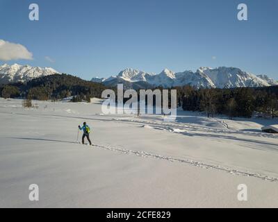 L'uomo cammina con le racchette da neve a Gerold in inverno, guardando verso i Monti Karwendel, cielo blu, piste da neve, alberi, Gerold, Krün, Foto Stock