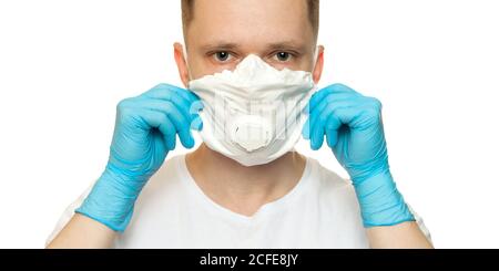 Giovane chirurgo medico in lattice guanti protettivi mette su maschera di protezione bianca su sfondo bianco. Uomo in guanti medici e sulla maschera protettiva per il viso. Foto Stock