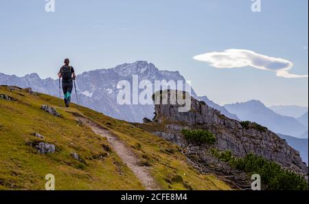 Giovane donna trekking verso Kramer con vista sui Monti Wetterstein (con Zugspitze), cielo blu, nuvole, sentiero escursionistico, roccia, Foto Stock