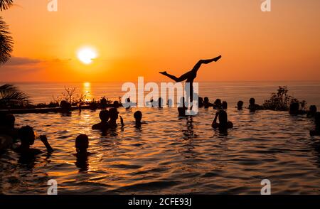 Giovane donna, giovane donna, giovane uomo, acrobazie, piscina infinity, piscina, tramonto, sole, festa in piscina, silhouette, mare, America Centrale, Costa Rica Foto Stock