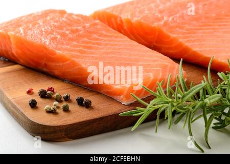 Due filetti di salmone freschi, grani di pepe e rosmarino fresco su un tagliere di legno marrone. Mangiare sano, ricetta di pesce ingrediente. Foto Stock