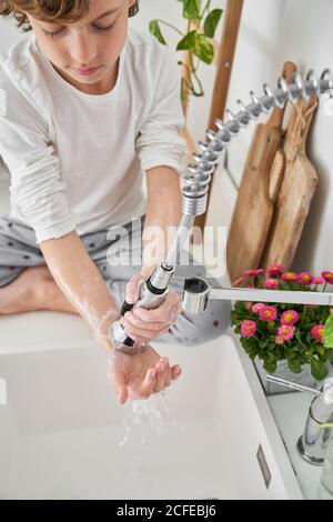 Biondo bambino lavando le sue mani nel lavello della cucina a. prevenire eventuali infezioni Foto Stock