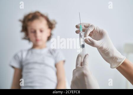 Crop mano in guanto di lattice di siringa anonima medico dimostrante con il farmaco di vaccino prima di dare l'iniezione al ragazzo Foto Stock