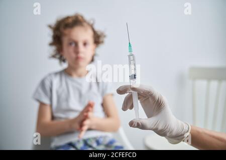 Crop mano in guanto di lattice di siringa anonima medico dimostrante con il farmaco di vaccino prima di dare l'iniezione al ragazzo Foto Stock