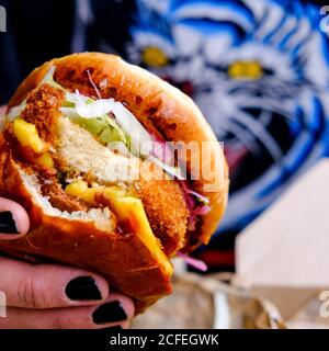 Persona con unghie verniciate nere che tiene UN Vegano fresco Burger a base di piante in un bun Foto Stock