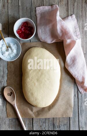 Da sopra pasta su carta da forno e ingredienti preparati per Cucina spagnola torta chiamato coca San Juan su tavolo di legno Foto Stock