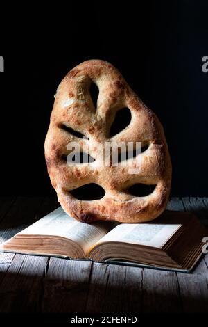 Pane di fougasse fresco posto su ricettario aperto su tavolo di legno su sfondo nero Foto Stock
