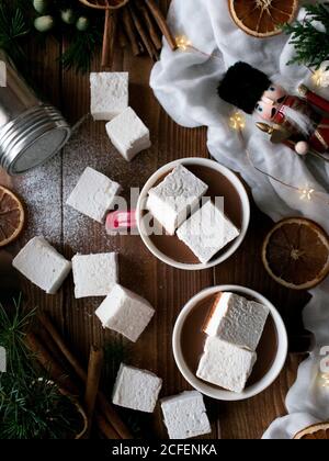 Bastoncini di cannella aromatica e citrus essiccati posti sul tavolo del legname vicino a tazze di gustoso cioccolato caldo con morbido marshmallows e. Varie decorazioni natalizie Foto Stock