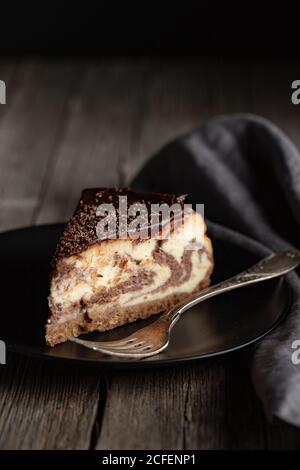 Pezzo di delizioso marmo fatto in casa o torta Zebra con cioccolato condimento servito su piatto nero con forchetta su legno scuro tabella Foto Stock