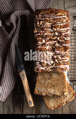 Vista dall'alto del pane fatto in casa a base di banana affettato con noci e zucchero a velo messo su tavola di legno con coltello e. tovaglia Foto Stock