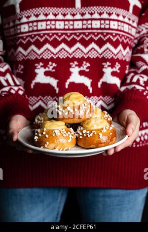 Crop femmina in rosso maglia natale e jeans piastra di tenuta con pasticceria fatta in casa e gustosi panini freschi di bianco spruzzare Foto Stock
