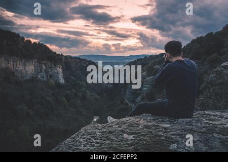 uomo con macchina fotografica seduto su collina montagna con magnifico cielo tramonto Foto Stock