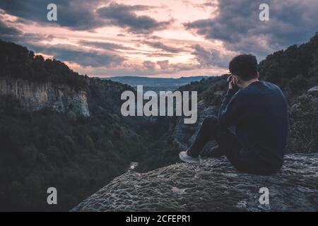 uomo con macchina fotografica seduto su collina montagna con magnifico cielo tramonto Foto Stock