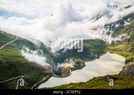 Fitte nuvole bianche che galleggiano su terreni verdi montagnosi con tranquillità lago in Austria Foto Stock