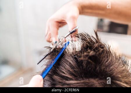 Vista posteriore di maschio irriconoscibile che fa un taglio di capelli a ragazzo usando forbici contro gli interni sfocati del bagno leggero a casa Foto Stock