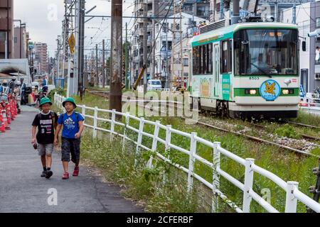 I ragazzi delle scuole elementari camminano accanto ad un tram o ad un'auto di strada sulla linea Toden Arakawa, conosciuta come il tram Tokyo Sakura, Tokyo Japan Foto Stock