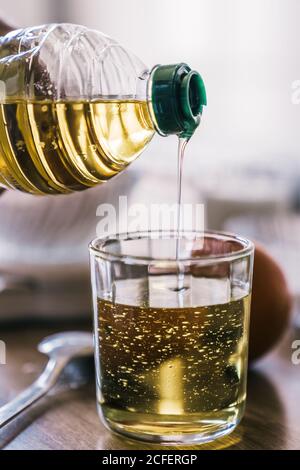 Raccolto femmina anonimo versando olio vegetale in vetro di misura messo a tavola con ingredienti per la ricetta mentre si prepara la pasta a. casa Foto Stock
