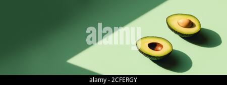 Avocado tagliato a metà su sfondo neo-menta. Banner Web con luce solare. Foto Stock