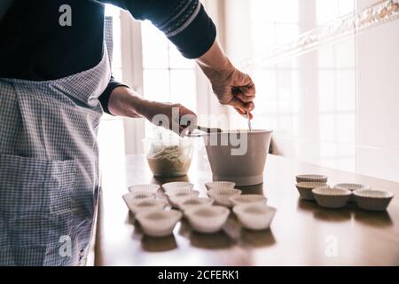 Vista laterale del prodotto femminile confettatore con grembiule in piedi cucina a casa e preparazione per versare l'impasto custodie di carta per muffin Foto Stock