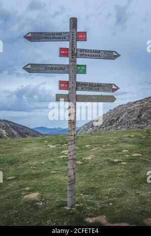 Palo in legno scablato con indicazioni stradali situato su una collina erbosa contro il cielo nuvoloso in natura Foto Stock