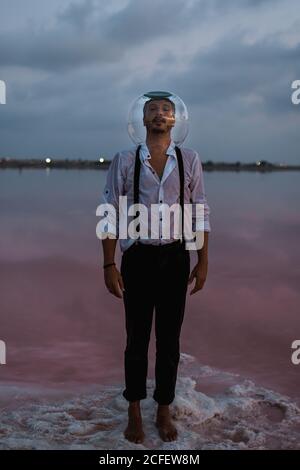 Uomo pusivo che guarda la macchina fotografica in camicia bagnata con vuoto aquarium a testa in piedi e contemplare da mare fermo in crepuscolo Foto Stock