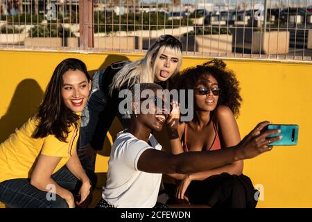 Allegro giovane e diverse amiche che prendono selfie sullo smartphone dentro via Foto Stock