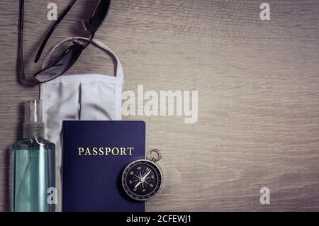 Viaggio sicuro durante una crisi pandemica, scrivania in legno con maschera chirurgica, mappa e altri accessori. Foto Stock