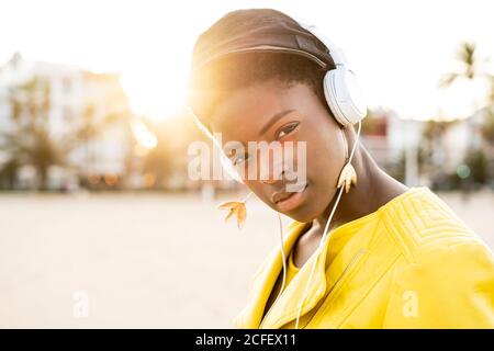 Ritratto di Afro American Woman in elegante giacca luminosa guardando la fotocamera su spiaggia sabbiosa sfondo sfocato Foto Stock