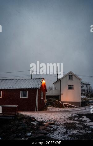 Cottage a strisce rosso scuro con finestre bianche e tetto innevato In piccola città in tempo sovrastato a Lofoten Foto Stock