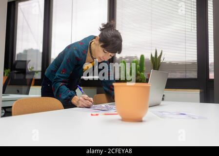Bella donna che lavora con i documenti mentre si è in piedi alla scrivania dentro ufficio moderno Foto Stock
