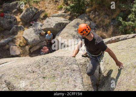 Dall'alto giovani avventurieri che arrampicano in montagna indossando imbracatura di sicurezza contro paesaggio pittoresco Foto Stock