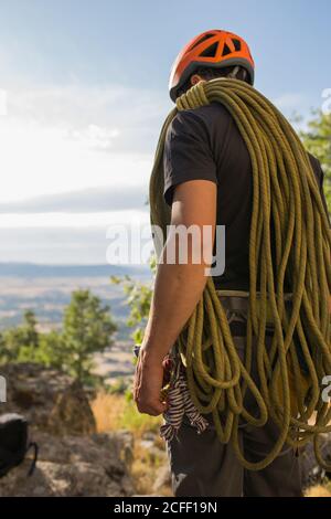 Dal basso, la vista posteriore dell'arrampicatore prepara la sua attrezzatura a. inizia a salire Foto Stock