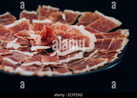 Dall'alto si vedano sottili fette di prosciutto con sego linee servite in piatto su sfondo nero Foto Stock