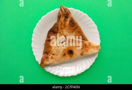 Famosa cucina tradizionale araba, mediorientale, israeliana. Spinaci Manakish su sfondo verde. Torta triangolare di spinaci su piatto bianco Foto Stock