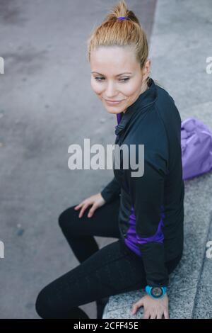 Giovane donna caucasica bionda con abbigliamento sportivo seduto in un marciapiede sulla strada Foto Stock