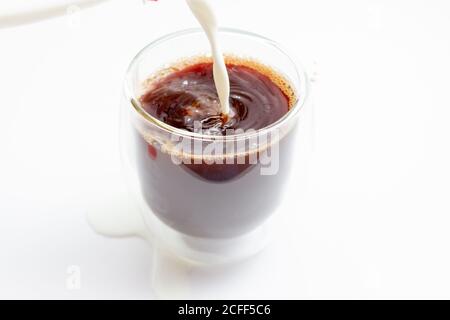 Versare il latte nel caffè freddo in una tazza di vetro bianca tabella Foto Stock