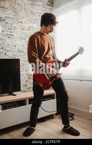 Uomo adulto a corpo pieno che suona la chitarra elettrica mentre si è in piedi camera accogliente a casa Foto Stock